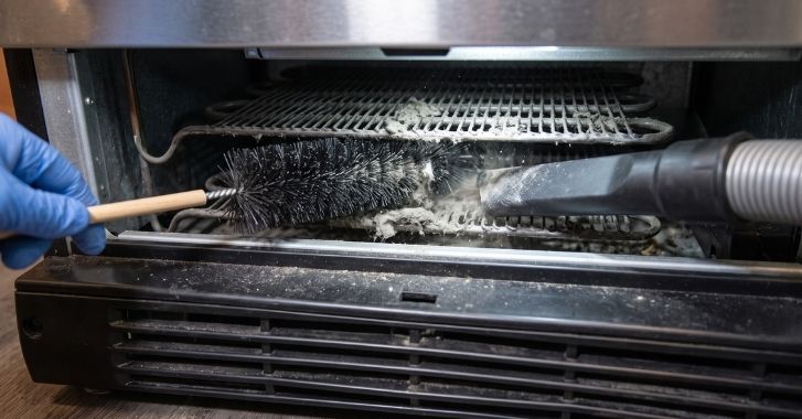 Coil brush and vacuum cleaning dusty refrigerator condenser coils behind a front grille